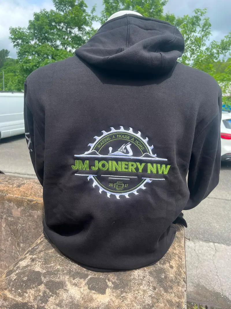 Black hoodie with the JM Joinery NW logo across the back