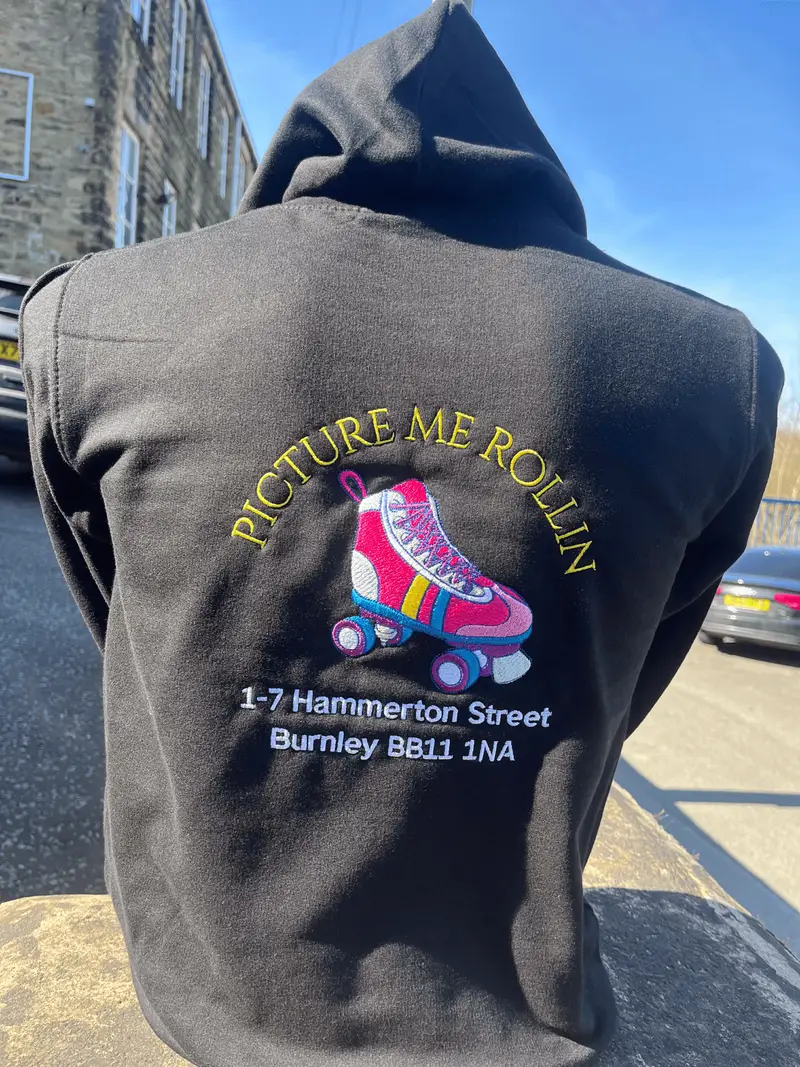 Black hoodie worn back to camera, embroidered with the Picture Me Rollin logo and the rink's Burnley address