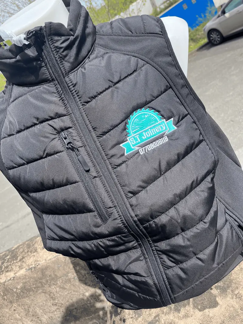 Black padded gilet embroidered with the S.T Joinery saw blade logo and phone number