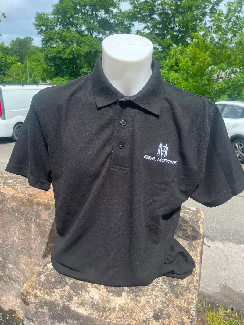 Black polo shirt embroidered with the Real Motors monogram in white thread