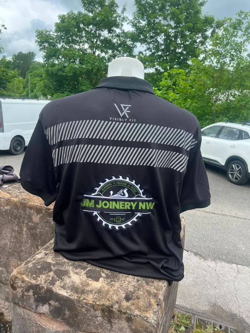 Black reflective polo shirt with the JM Joinery NW logo on the back