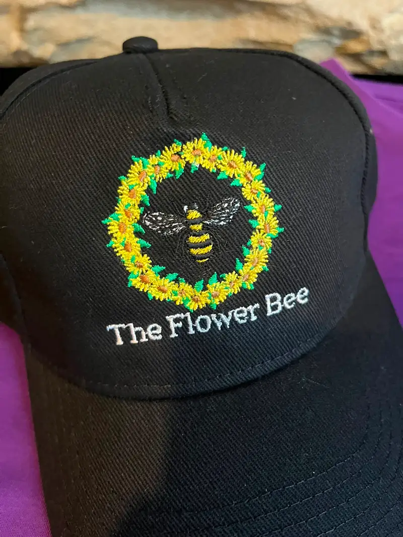 Close-up of a bee and sunflower wreath embroidered on a black cap for The Flower Bee, stitched at the ThreeKZ workshop in Colne