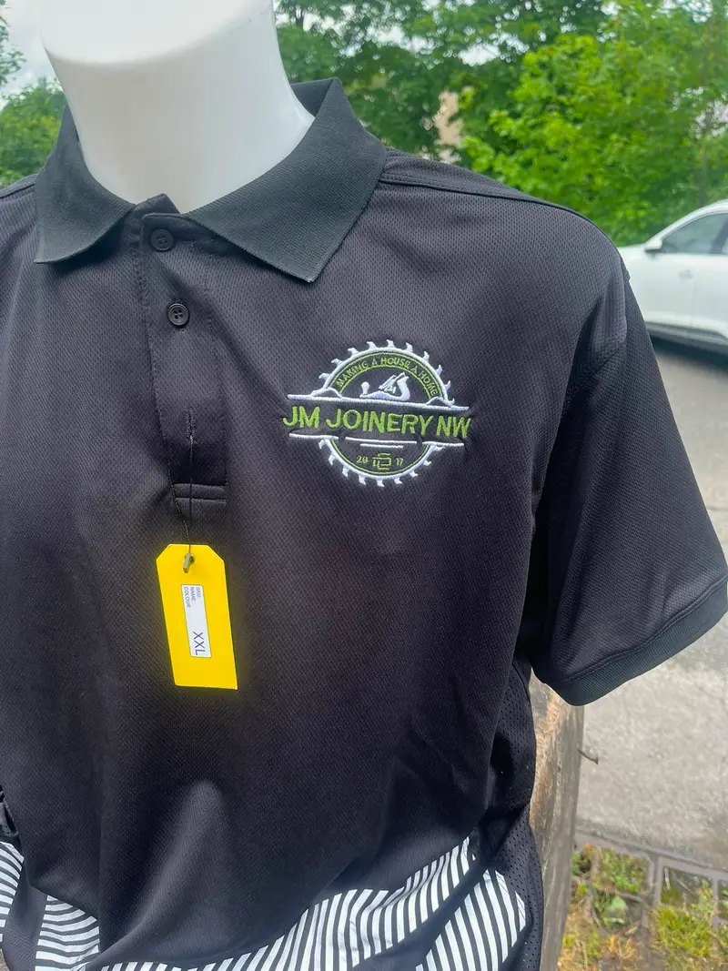 Close-up of the JM Joinery NW logo embroidered on a black polo shirt