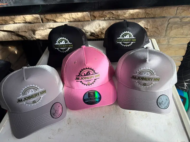 Five trucker caps in black, grey and pink, each embroidered with the JM Joinery NW logo