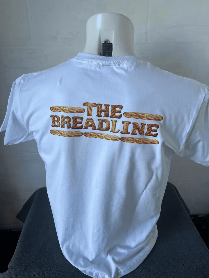 White t-shirt printed with The Breadline bakery logo framed by baguettes